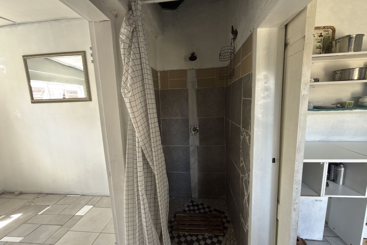 A compact shower area featuring tiled walls and built-in shelving, currently showing signs of incomplete finishes and dated infrastructure.