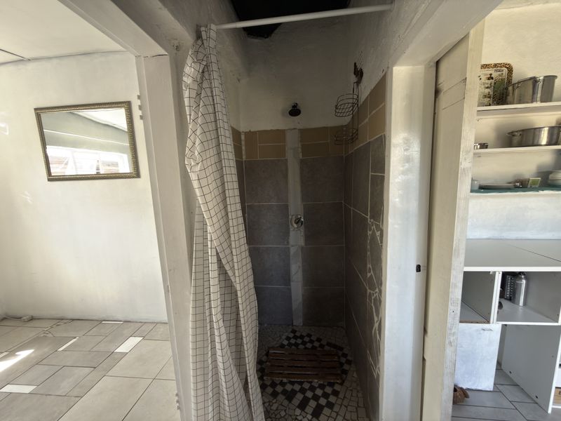 A compact shower area featuring tiled walls and built-in shelving, currently showing signs of incomplete finishes and dated infrastructure.