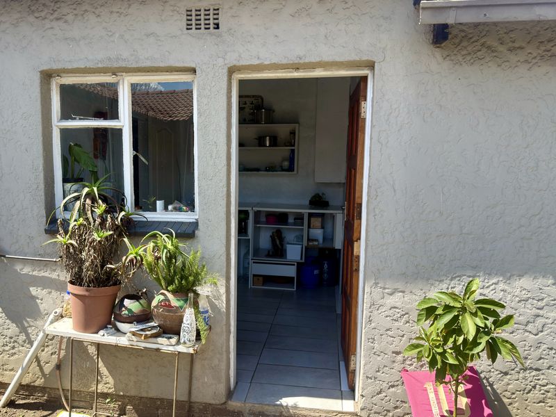 Exterior view of a utility or scullery area featuring tiled flooring and built-in shelving, accessible via a timber door from the rear garden.