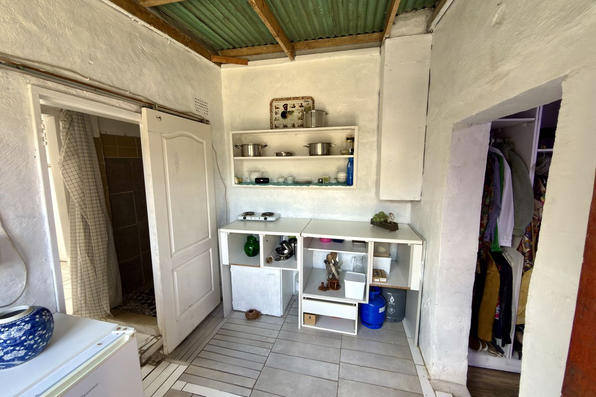 A compact kitchen area featuring tiled flooring, built-in shelving, and an exposed corrugated roof structure, providing a basic functional space.