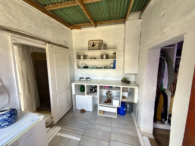 A compact kitchen area featuring tiled flooring, built-in shelving, and an exposed corrugated roof structure, providing a basic functional space.