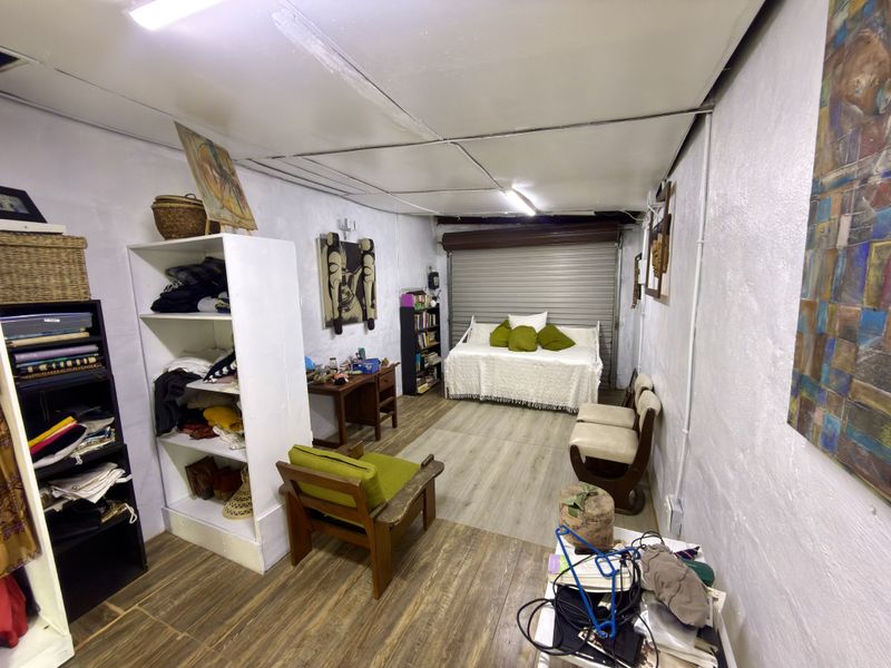 Converted garage space featuring laminate flooring, roller shutter door, and basic fluorescent lighting, currently utilized as a multi-purpose living area.