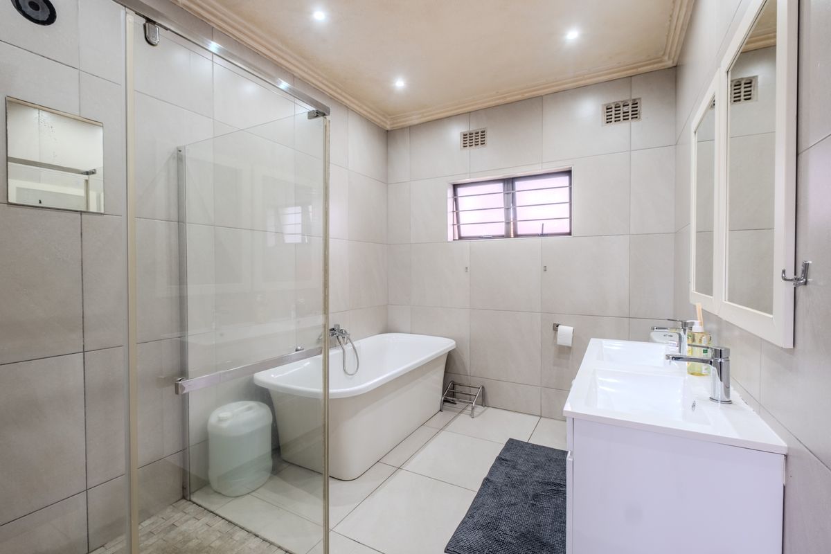 Modern bathroom featuring a freestanding bathtub, glass-enclosed shower, and a double vanity with contemporary fixtures and neutral floor-to-ceiling tiling.