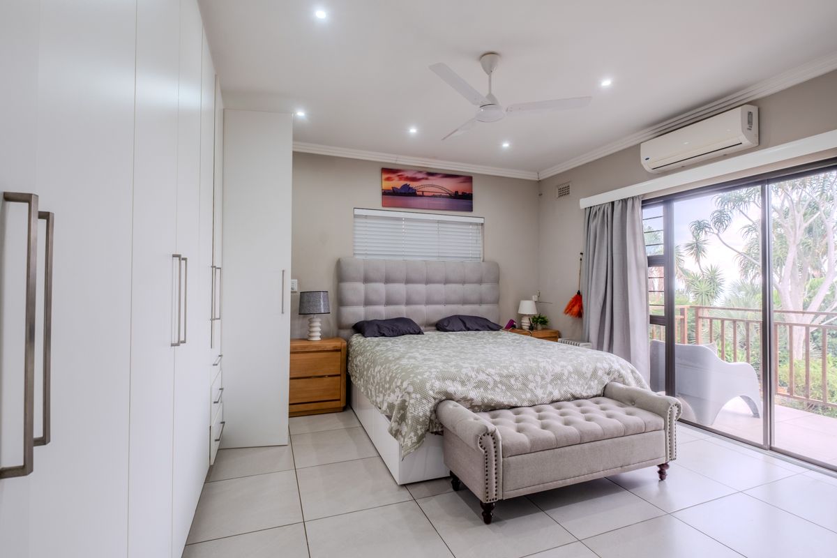 A well-maintained bedroom featuring built-in cupboards, tiled flooring, air conditioning, and a sliding glass door leading to an outdoor balcony.