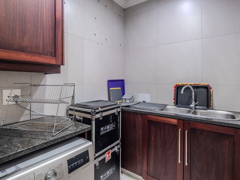 Compact scullery area featuring dark wood cabinetry, granite countertops, and a double stainless steel sink with tiled wall finishes.