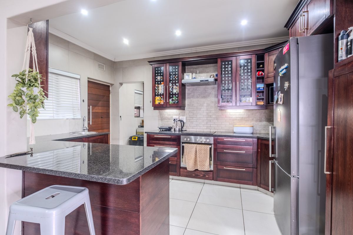 A well-maintained kitchen featuring dark wood cabinetry, granite countertops, built-in oven, electric hob, and modern tiled flooring with recessed lighting.