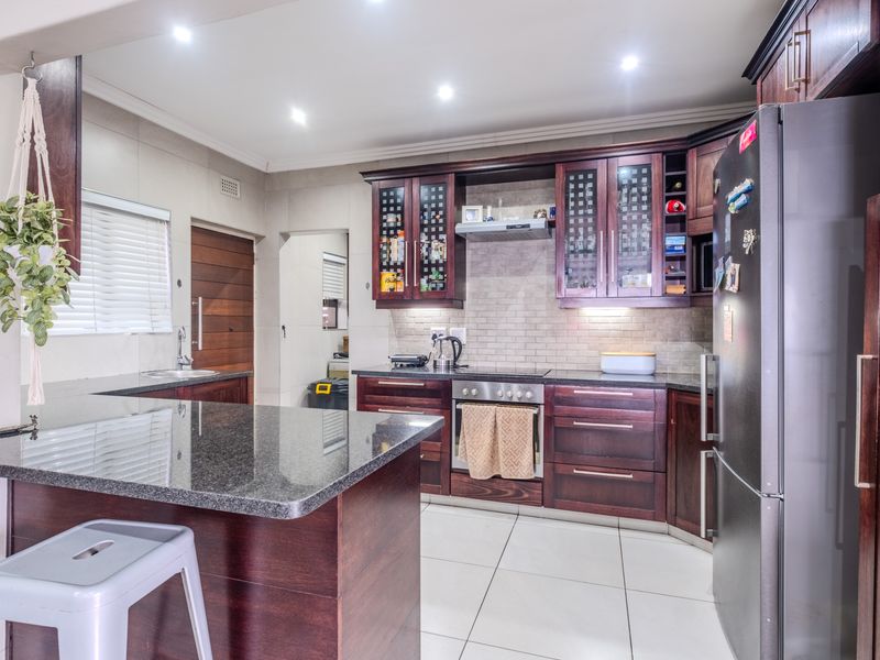 A well-maintained kitchen featuring dark wood cabinetry, granite countertops, built-in oven, electric hob, and modern tiled flooring with recessed lighting.