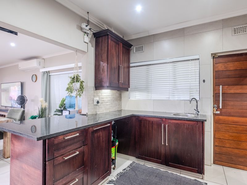 A functional kitchen featuring dark wood cabinetry, granite countertops, and a tiled splashback, seamlessly connected to the adjacent living area.