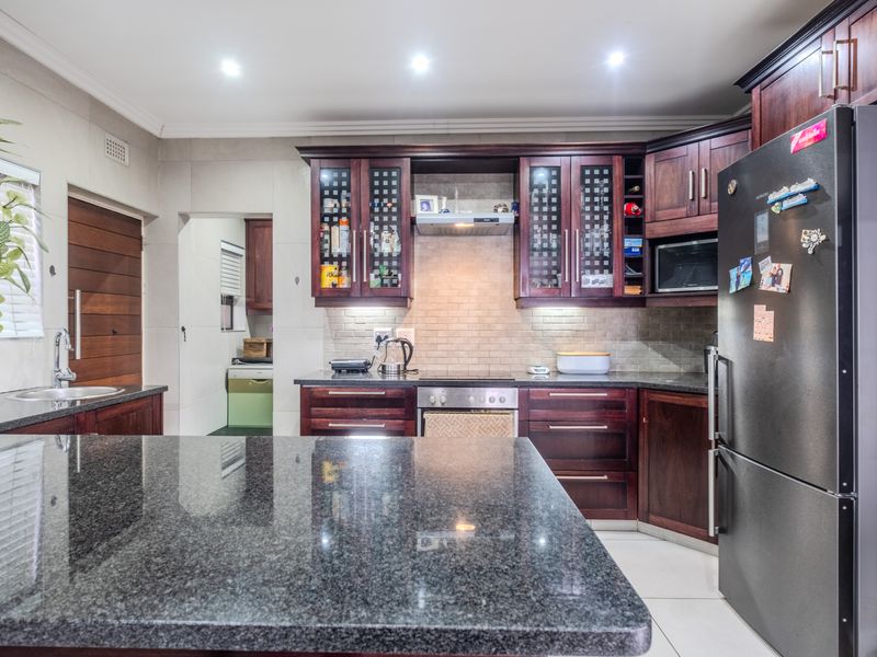A well-appointed kitchen featuring dark wood cabinetry, granite countertops, a tiled backsplash, and integrated appliances, including an oven, hob, and extractor fan.