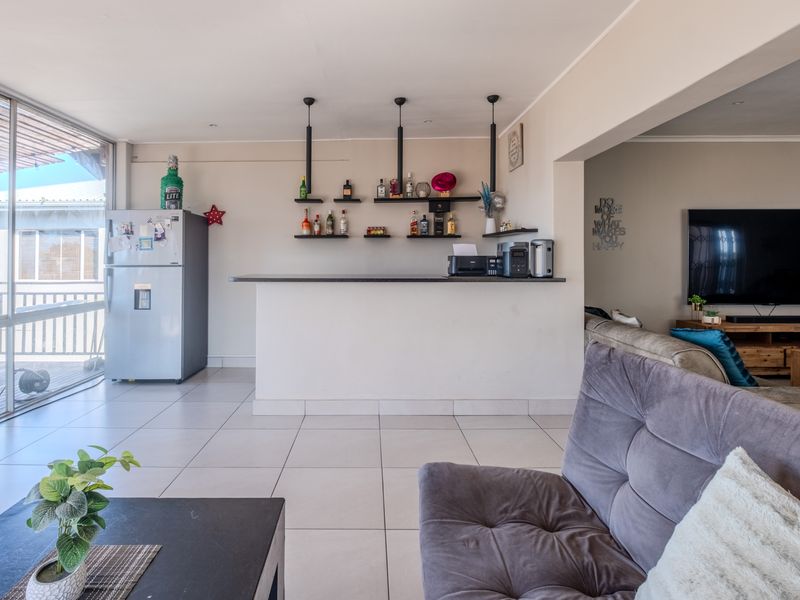 A well-lit open plan living area featuring a built-in bar counter with floating shelving and direct access to an outdoor balcony through sliding doors.