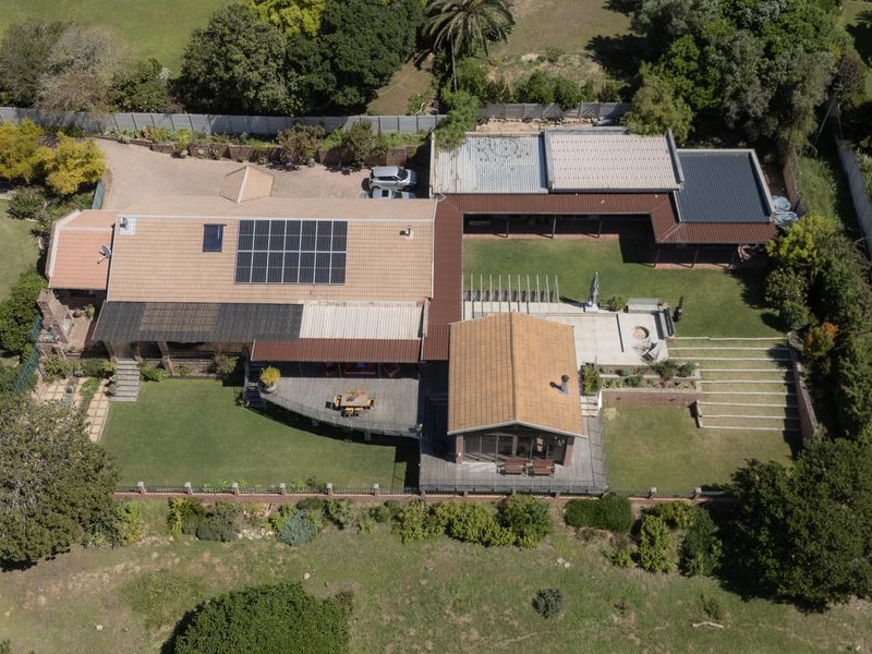 Aerial view of a residential property featuring a large tiled roof with solar panels, extensive timber decking, landscaped gardens, and tiered outdoor entertainment areas.
