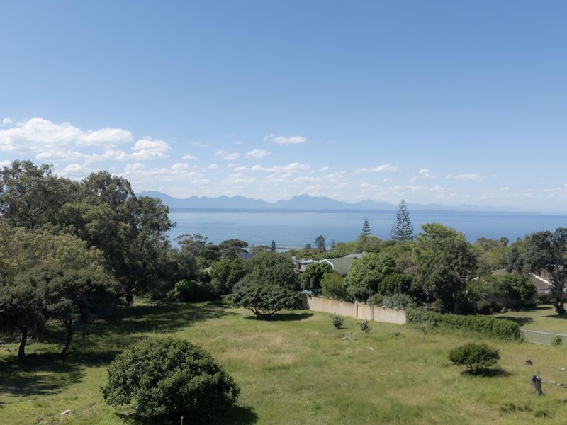 An elevated scenic view overlooking a grassy garden area, mature trees, and a distant coastal landscape with mountains.