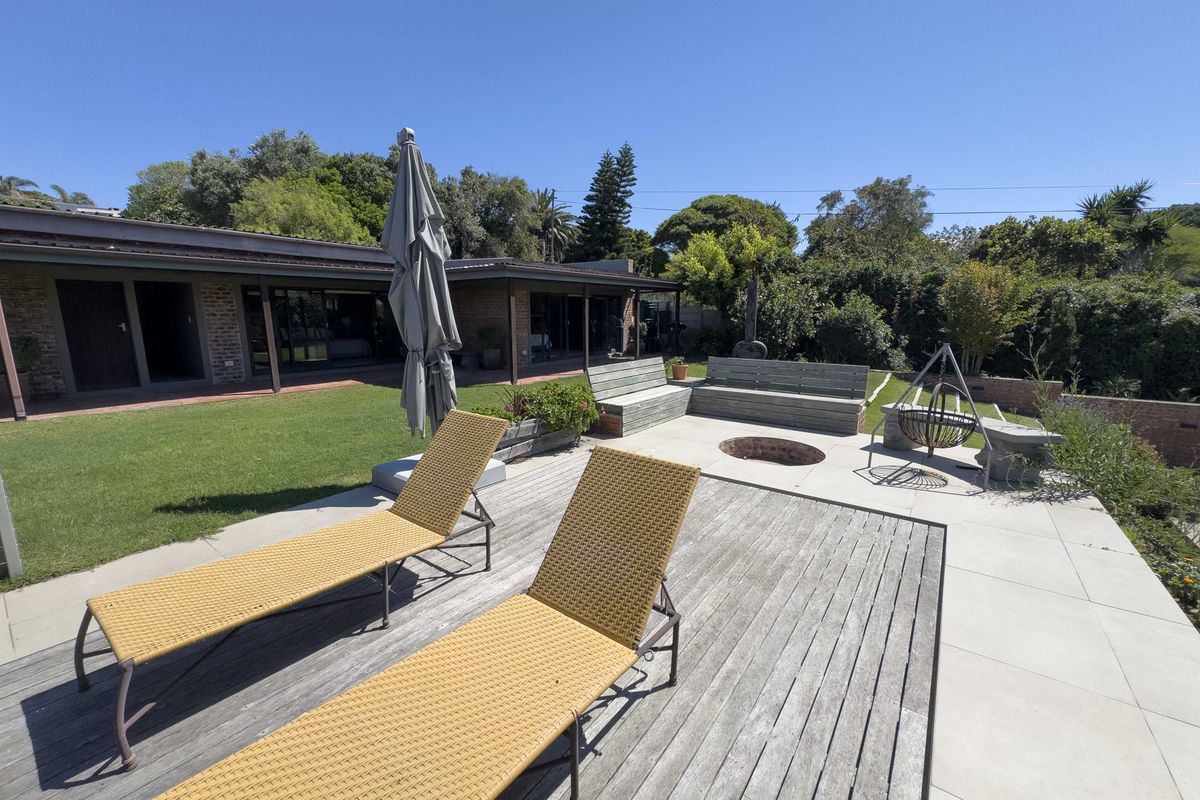 Spacious rear garden featuring a timber deck, paved patio area with a built-in fire pit, and integrated bench seating overlooking the lawn.