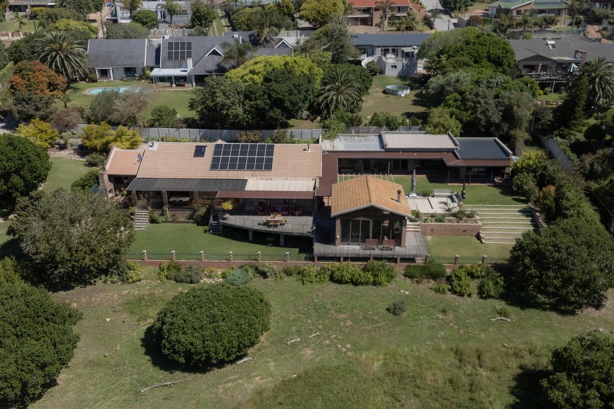 Aerial view of a residential property featuring a large tiled roof with solar panels, expansive decking, and a well-maintained garden area.