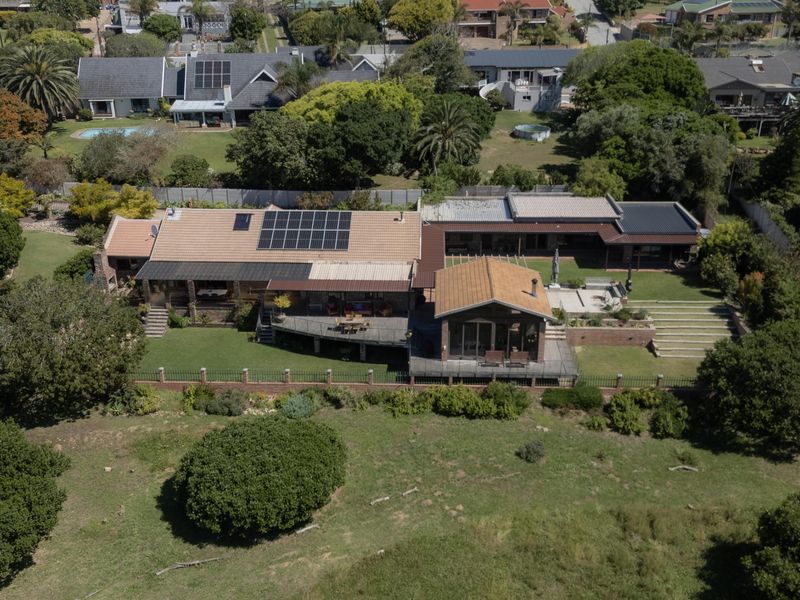 Aerial view of a residential property featuring a large tiled roof with solar panels, expansive decking, and a well-maintained garden area.