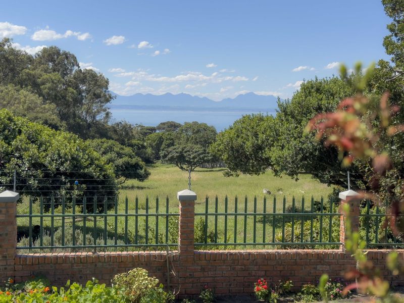 Scenic view overlooking a lush green landscape with distant mountains and ocean, framed by a brick and metal boundary fence.