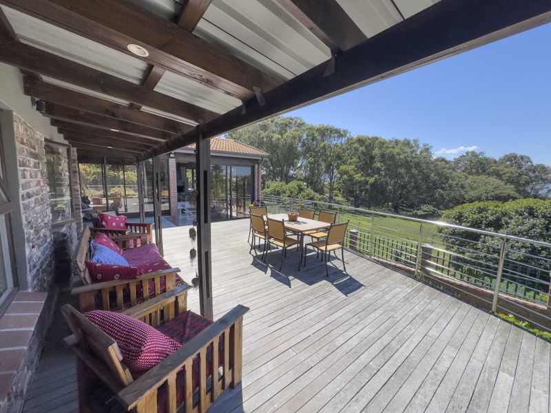 Spacious outdoor timber deck featuring a covered pergola, stainless steel balustrade, and views over the surrounding garden and landscape.