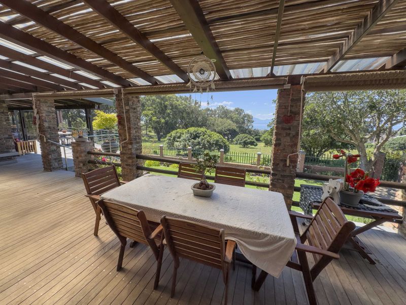 Spacious covered patio featuring timber decking, exposed brick pillars, and a bamboo slat roof, offering scenic garden and landscape views.