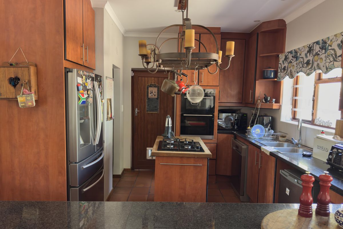 A functional kitchen featuring warm-toned wooden cabinetry, granite countertops, a central island with a gas hob, and a built-in double oven.