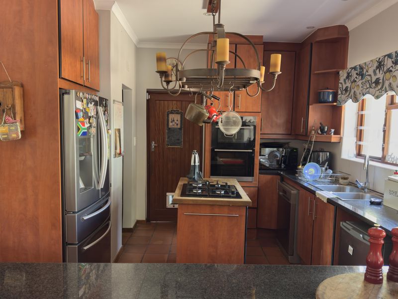 A functional kitchen featuring warm-toned wooden cabinetry, granite countertops, a central island with a gas hob, and a built-in double oven.