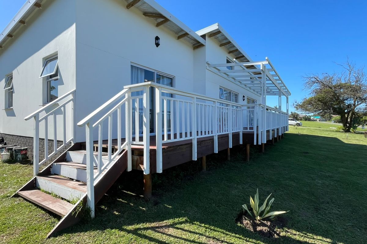 A rear view of the house featuring an elevated timber deck with a pergola, white balustrades, and sliding glass door access to the interior.