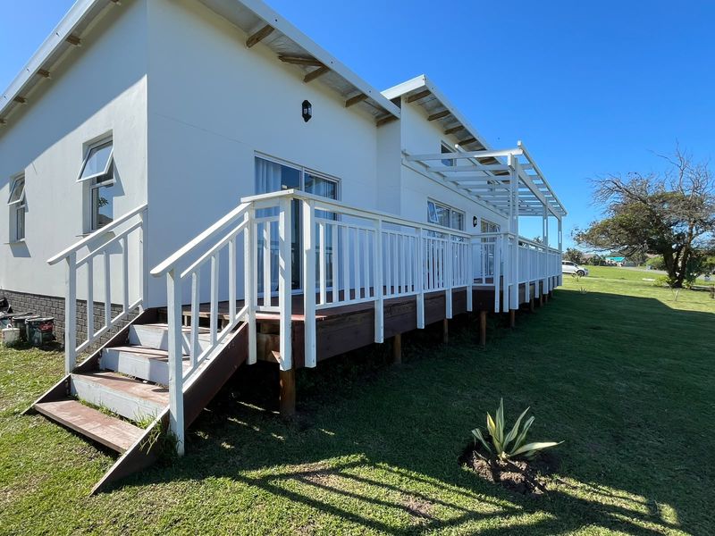 A rear view of the house featuring an elevated timber deck with a pergola, white balustrades, and sliding glass door access to the interior.