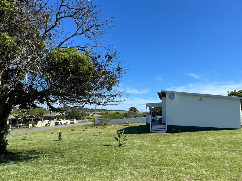 A view of the rear exterior of the house featuring a large lawn, boundary fencing, and a raised deck area with stairs.