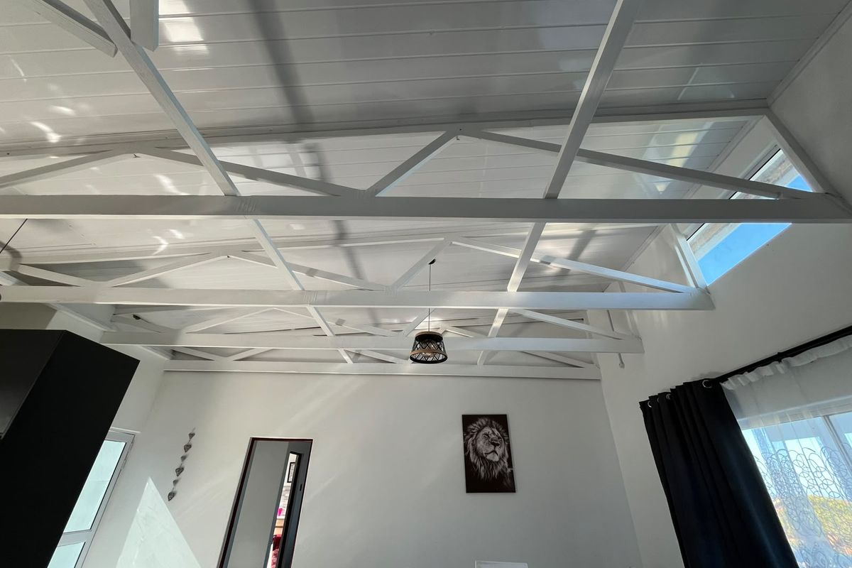 Bright living area featuring a high vaulted ceiling with exposed white-painted timber trusses and clerestory windows that provide ample natural light.