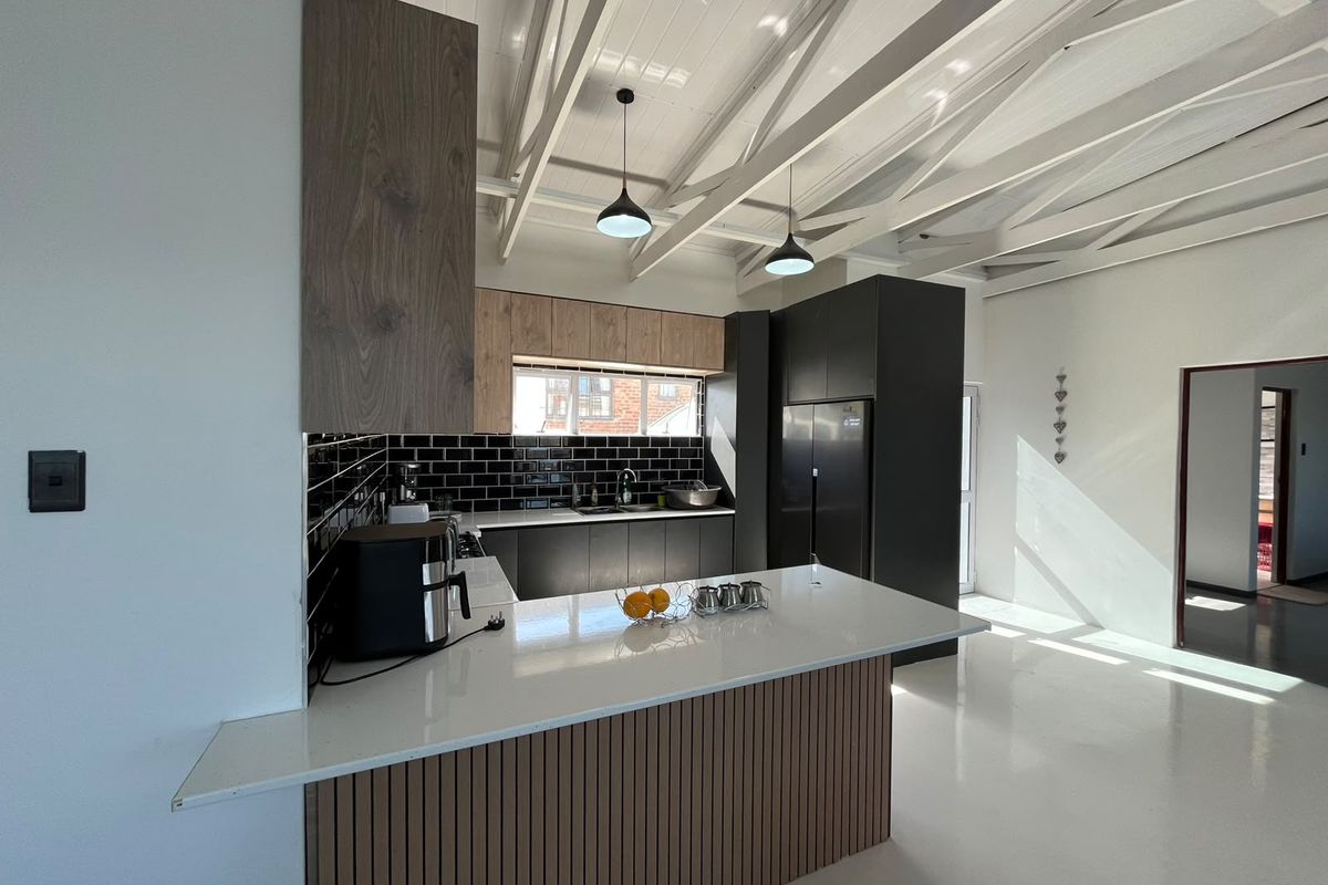 Modern kitchen featuring a central island with quartz countertops, sleek cabinetry, subway tile backsplash, and striking exposed white-painted timber ceiling beams.