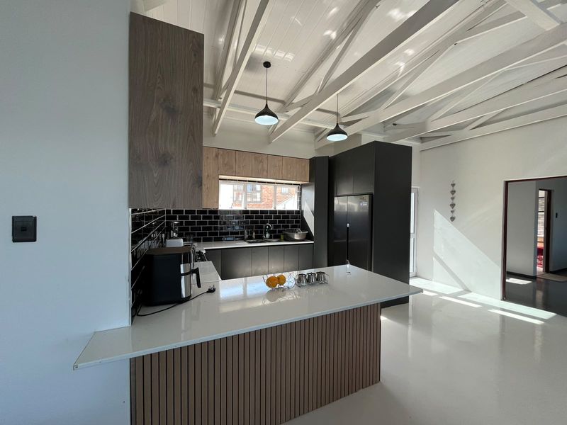 Modern kitchen featuring a central island with quartz countertops, sleek cabinetry, subway tile backsplash, and striking exposed white-painted timber ceiling beams.
