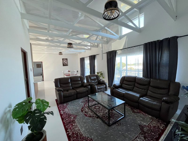 Spacious open-plan living area featuring a high vaulted ceiling with exposed white trusses, tiled floors, and large sliding doors providing ample natural light.