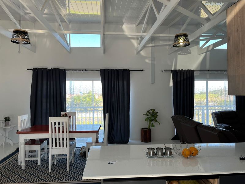 Spacious open-plan living and dining area featuring high vaulted ceilings with exposed white trusses, skylights, and a modern kitchen island with stone countertops.