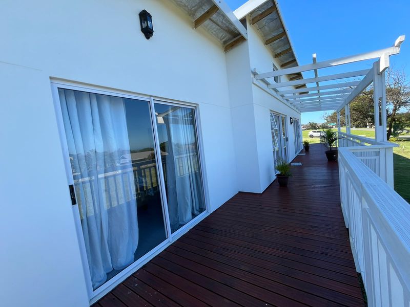 A spacious elevated timber deck featuring a pergola, sliding glass doors, and white railings, offering a clean outdoor living space.