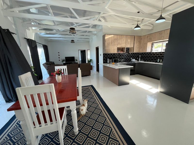 Spacious open-plan living and dining area featuring a modern kitchen with island, subway tile backsplash, and striking exposed white roof trusses.