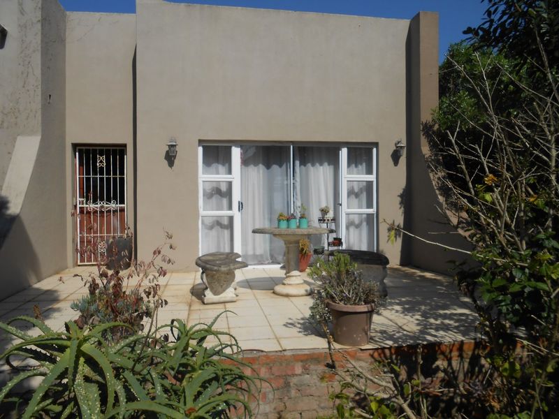 A paved outdoor patio area featuring sliding glass doors, a security gate, and exterior wall lighting, set against a neutral-toned building facade.