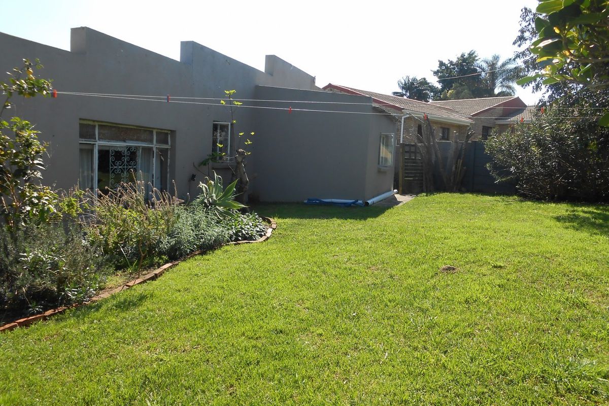Rear view of the property featuring a plastered masonry facade, steel-framed windows with security gates, and a well-maintained lawn with brick-edged garden beds.