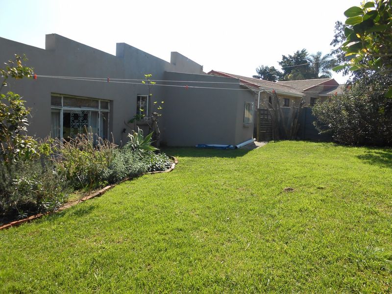 Rear view of the property featuring a plastered masonry facade, steel-framed windows with security gates, and a well-maintained lawn with brick-edged garden beds.