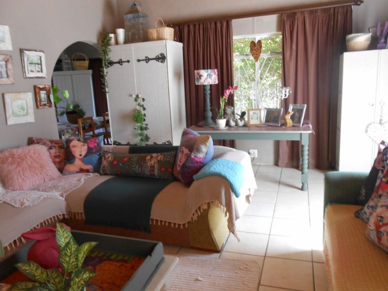 A cozy living room featuring tiled flooring, an arched entryway leading to an adjacent space, and large windows fitted with security burglar bars.