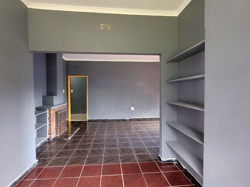 An empty living area featuring dark tiled flooring, built-in shelving units, and a traditional brick fireplace, offering a versatile space for customization.