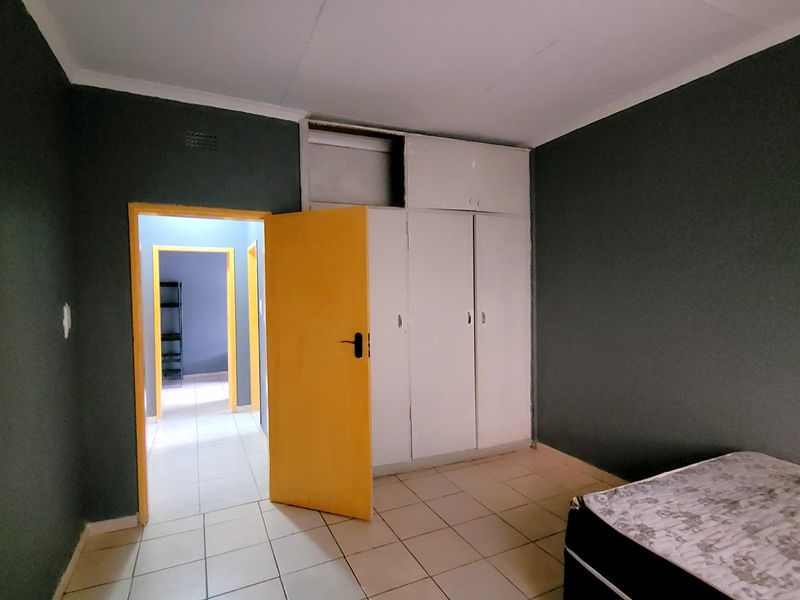 A bedroom featuring tiled flooring and built-in cupboards, with direct access to a hallway.