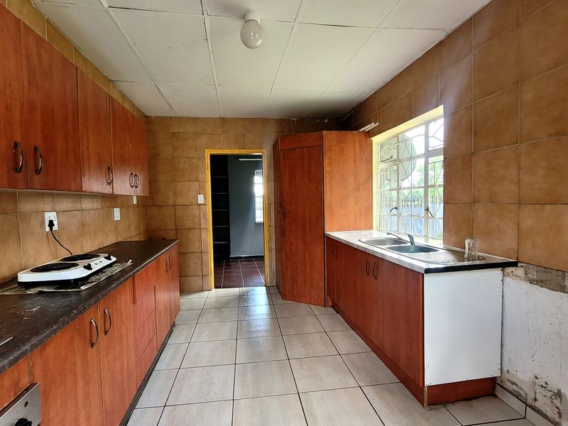 A dated kitchen featuring wooden cabinetry, tiled splashbacks, and a double bowl sink, requiring cosmetic updates and repairs to the wall finishes.