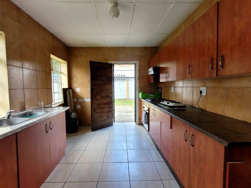 A functional kitchen featuring built-in cabinetry, tiled splashbacks, and tiled flooring, offering a blank canvas for potential modern updates and renovation.