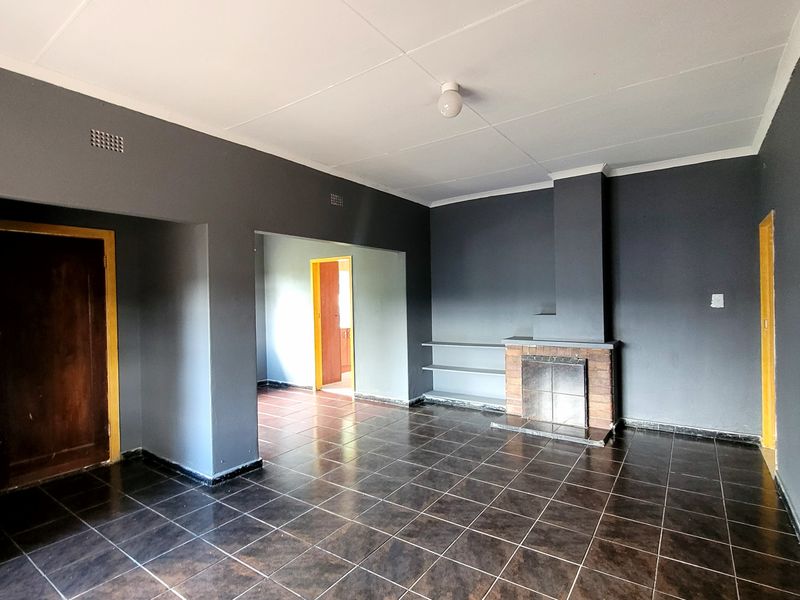 Spacious living room featuring dark tiled flooring, a brick fireplace, and built-in shelving, offering a blank canvas for interior design.