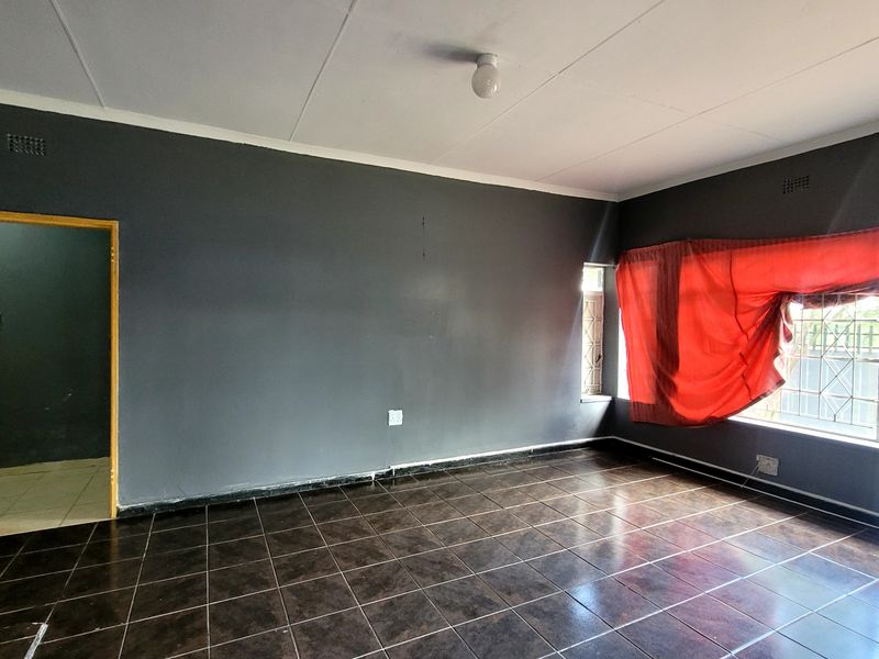 An empty living room featuring dark tiled flooring, grey painted walls, and security bars on the window, offering a blank canvas for interior design.
