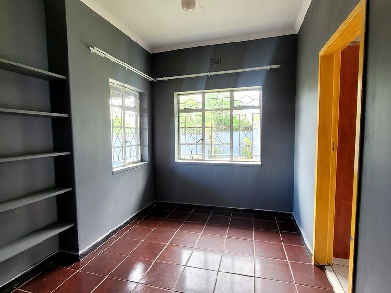 An empty bedroom featuring dark grey walls, tiled flooring, and built-in shelving units with security bars on the windows.