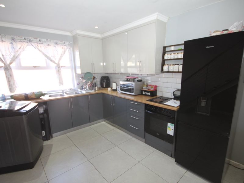Modern kitchen featuring grey and white cabinetry, subway tile backsplash, wooden countertops, and integrated appliances, offering a clean and functional cooking space.