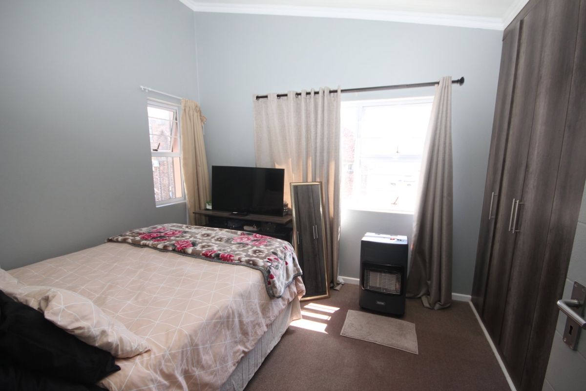 A well-lit bedroom featuring built-in cupboards, carpeted flooring, and dual windows with curtain rods.