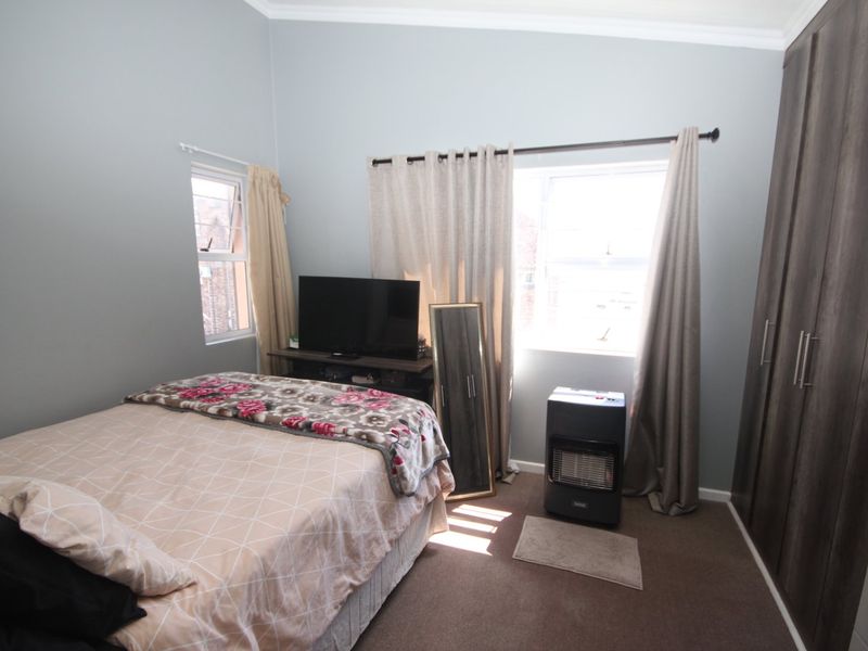 A well-lit bedroom featuring built-in cupboards, carpeted flooring, and dual windows with curtain rods.
