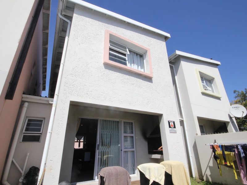 Rear elevation of a two-story apartment featuring a covered patio area with a built-in braai and sliding door access.