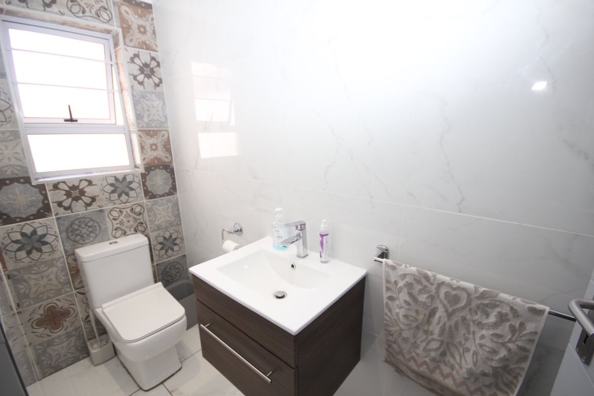 A modern bathroom featuring a wall-mounted vanity with basin, a sleek toilet, and decorative patterned wall tiles surrounding the window.